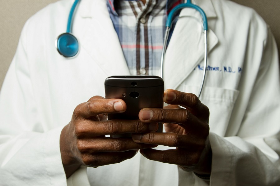 doctor wearing lavatory grown with green stethoscope on neck using phone while standing