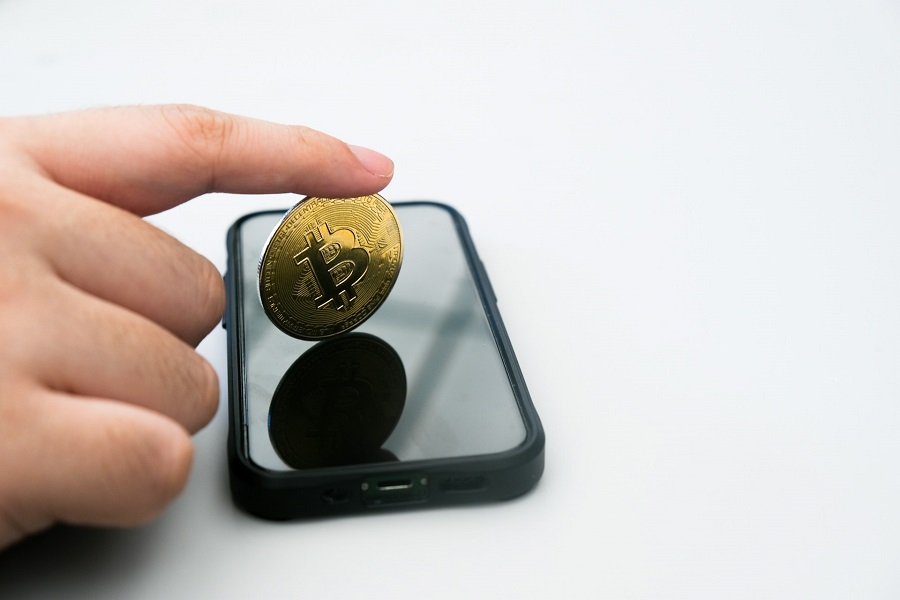 a person holding a gold coin in front of a cell phone
